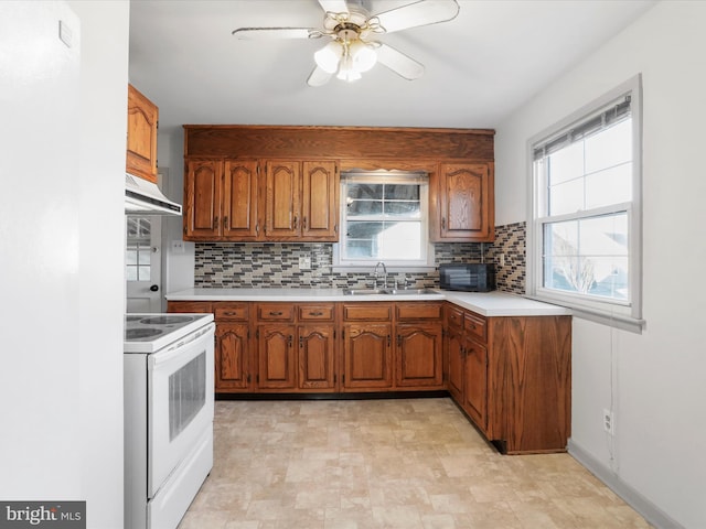 kitchen with under cabinet range hood, light countertops, white electric range oven, brown cabinetry, and a sink