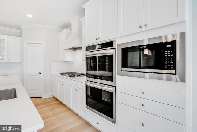 kitchen with light wood finished floors, ornamental molding, stainless steel appliances, light countertops, and custom range hood