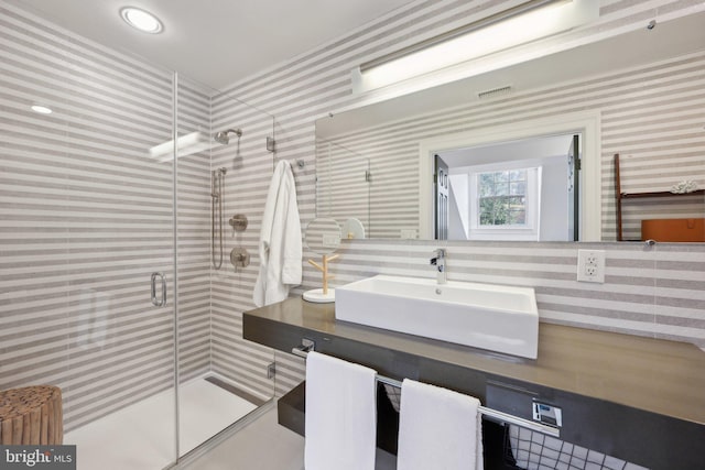 bathroom featuring a sink, visible vents, a shower stall, and wallpapered walls