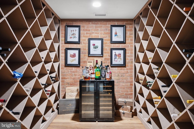 wine cellar featuring visible vents, wood finished floors, beverage cooler, and brick wall