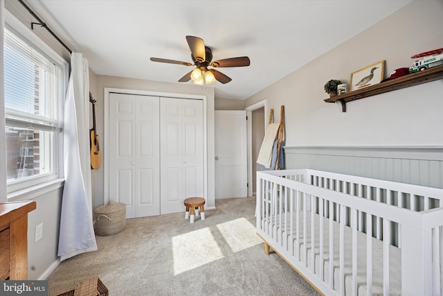 carpeted bedroom featuring a closet, a crib, ceiling fan, and wainscoting