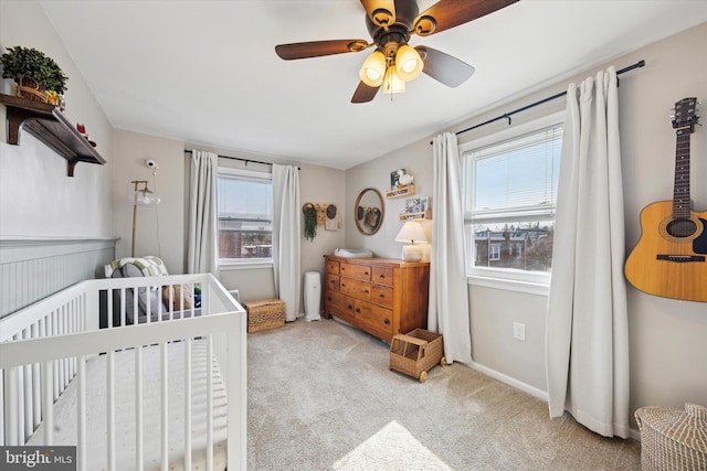 bedroom featuring a ceiling fan, multiple windows, a nursery area, and light colored carpet