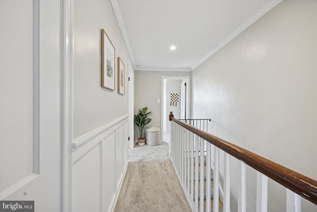 hall with a wainscoted wall, an upstairs landing, ornamental molding, carpet, and a decorative wall