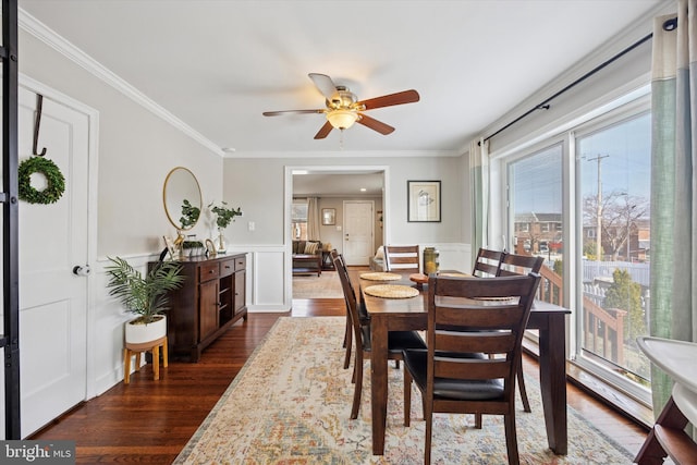 dining area with a wainscoted wall, ceiling fan, dark wood-style flooring, and ornamental molding