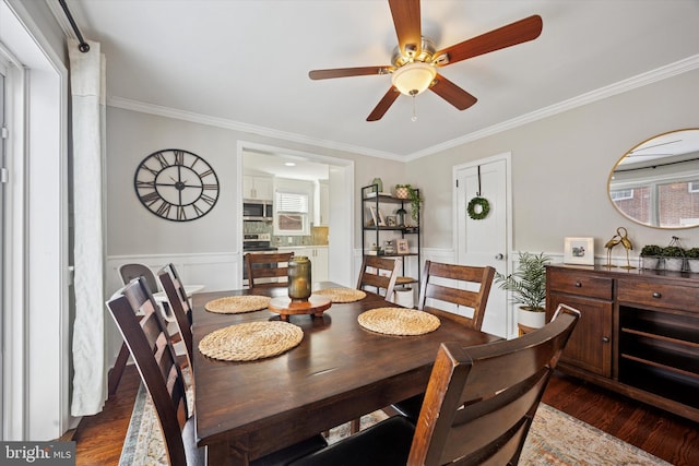 dining area featuring wainscoting, dark wood-type flooring, a ceiling fan, and ornamental molding