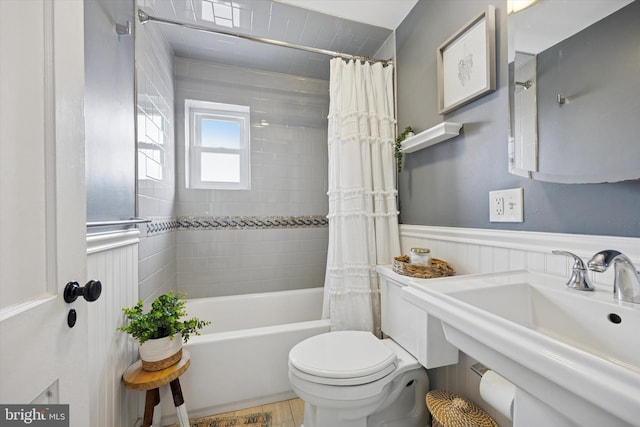 full bath featuring wainscoting, shower / bathtub combination with curtain, toilet, and a sink