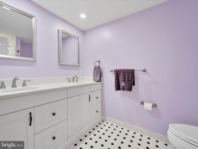 bathroom with double vanity, toilet, baseboards, and a sink