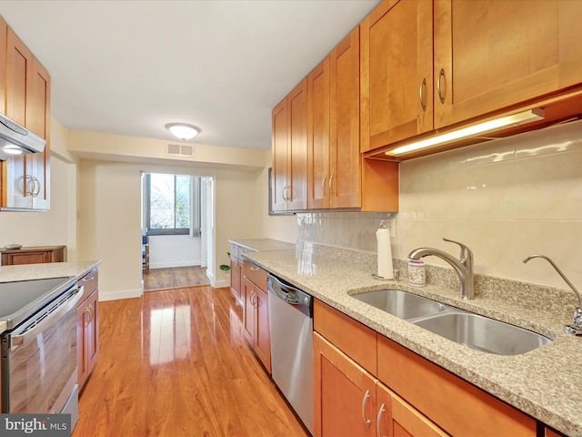 kitchen with tasteful backsplash, light wood finished floors, brown cabinetry, stainless steel appliances, and a sink