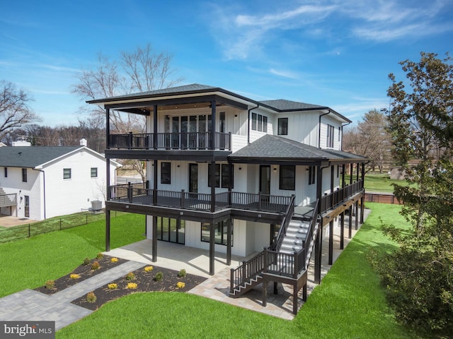 rear view of property with stairway, roof with shingles, board and batten siding, a patio area, and a lawn