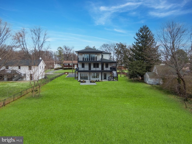 rear view of property featuring a yard, fence, a balcony, and stairway