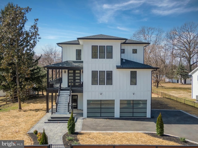 view of front of house with fence, driveway, a shingled roof, stairs, and board and batten siding