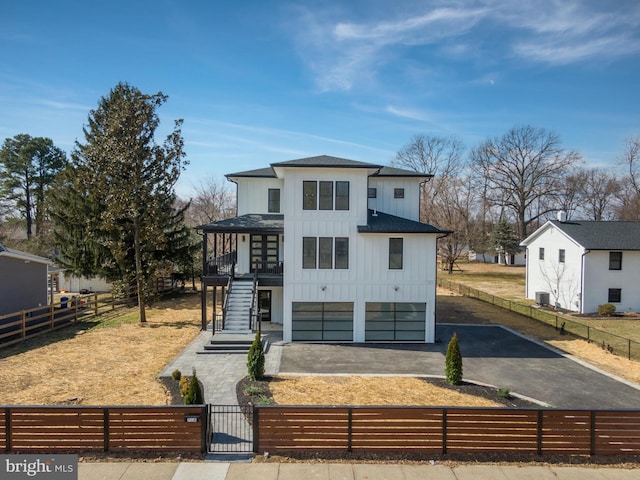 view of front of property with a fenced front yard, aphalt driveway, board and batten siding, a shingled roof, and central AC unit