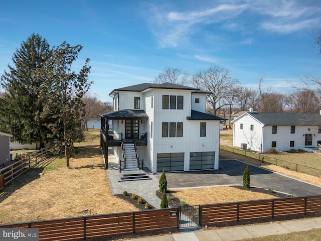 view of front of property featuring board and batten siding, a fenced front yard, stairs, driveway, and a gate