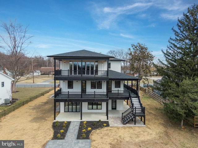 view of front facade featuring a fenced backyard, stairway, a patio, and roof with shingles