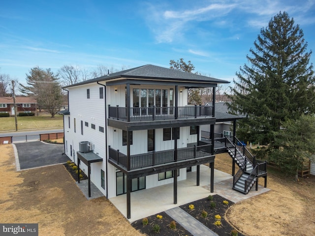 rear view of house with cooling unit, a shingled roof, stairs, a patio area, and board and batten siding