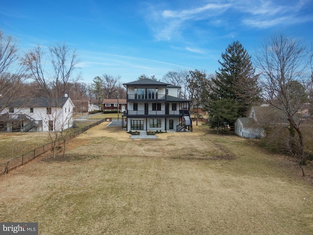 rear view of property featuring a lawn, stairs, a balcony, and fence