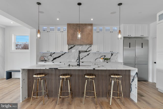 kitchen with tasteful backsplash, light wood-type flooring, a large island with sink, white cabinetry, and built in fridge