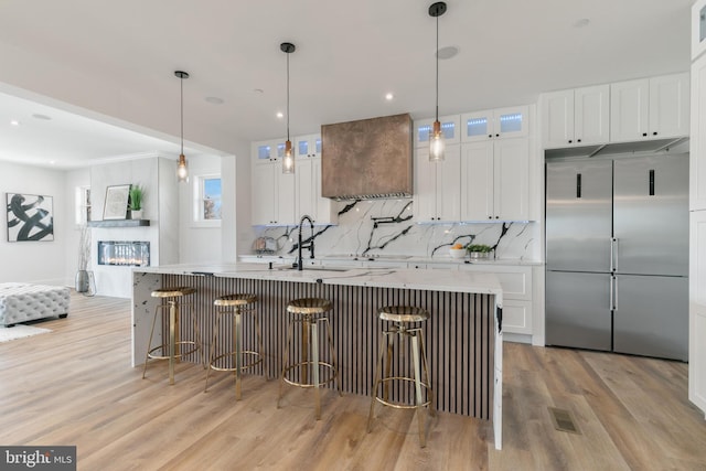 kitchen featuring a sink, premium range hood, white cabinets, and light countertops