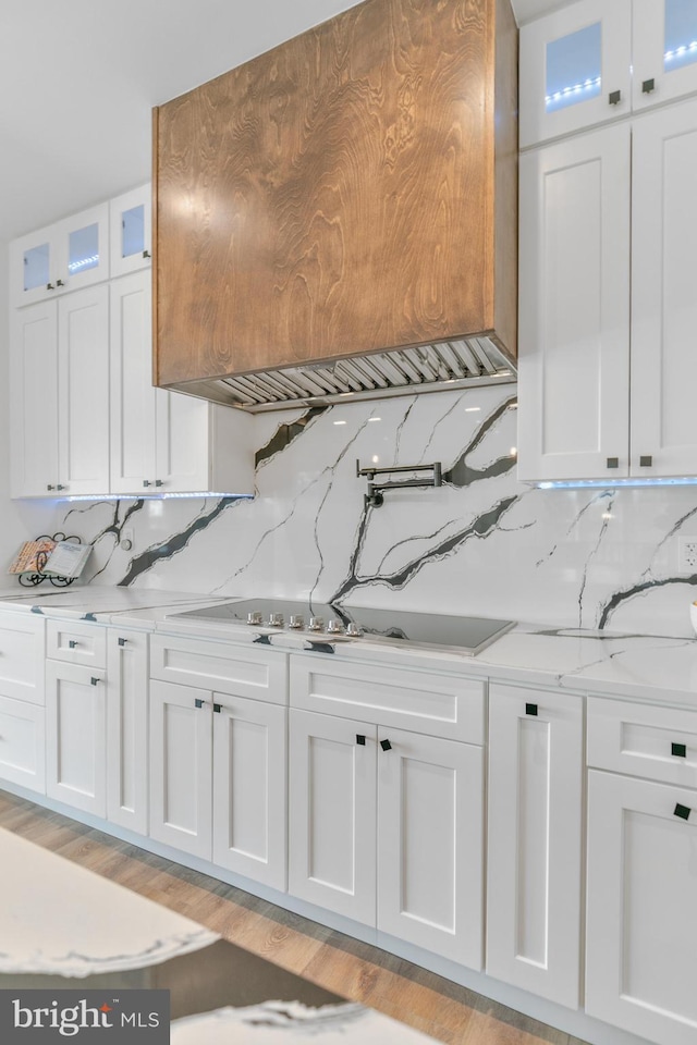 kitchen with tasteful backsplash, white cabinets, light wood finished floors, glass insert cabinets, and light stone countertops