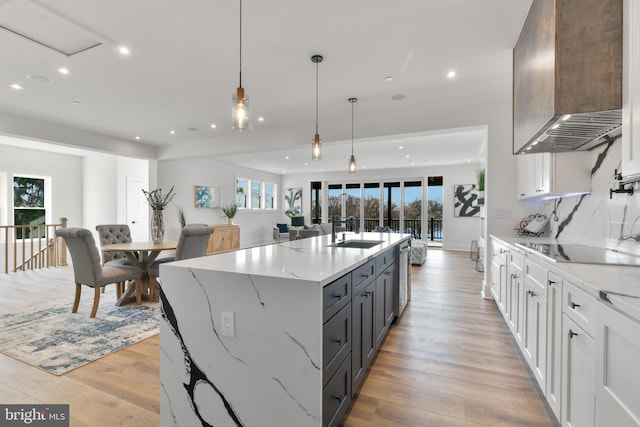 kitchen with light stone countertops, light wood-type flooring, black electric stovetop, wall chimney range hood, and open floor plan