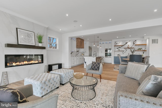 living room with a glass covered fireplace, recessed lighting, visible vents, and light wood-type flooring