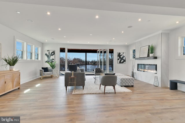 living room with recessed lighting, a wealth of natural light, light wood-style floors, and a glass covered fireplace