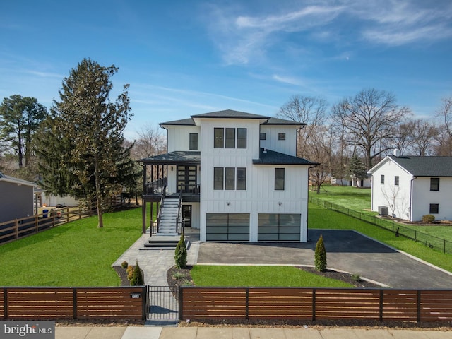 rear view of house featuring board and batten siding, a fenced front yard, stairs, a yard, and driveway