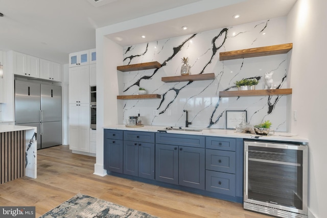 bar featuring beverage cooler, light wood-style flooring, stainless steel appliances, decorative backsplash, and a sink