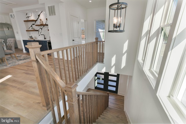 staircase featuring a notable chandelier, wood finished floors, visible vents, and baseboards