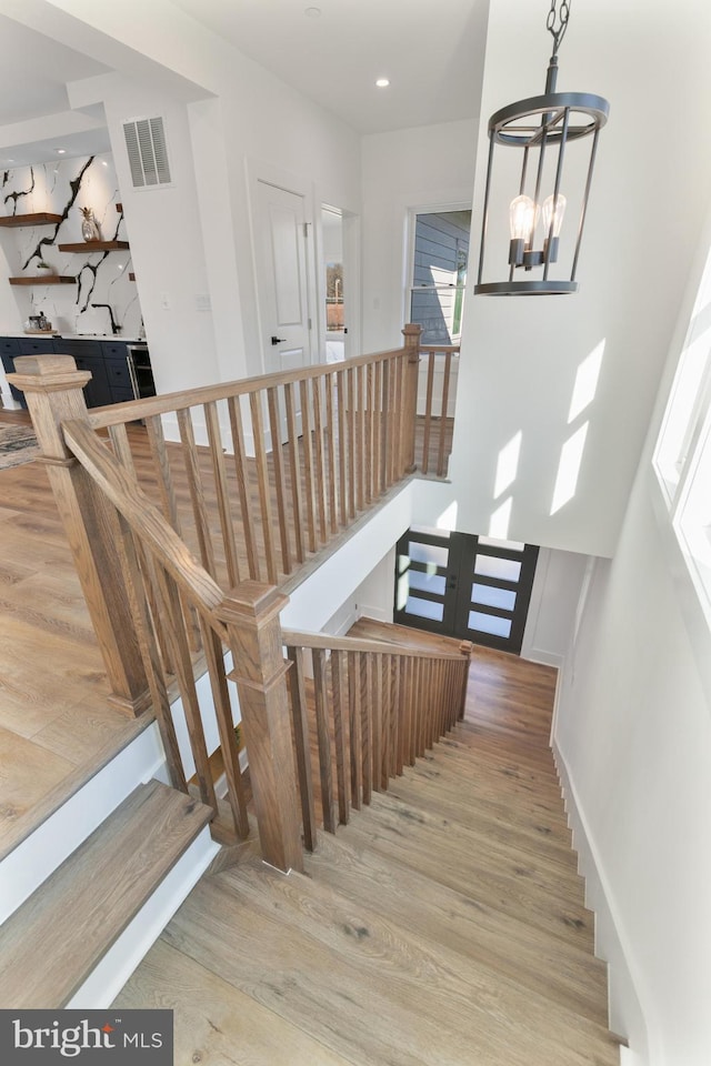 stairs featuring visible vents, baseboards, recessed lighting, an inviting chandelier, and wood finished floors