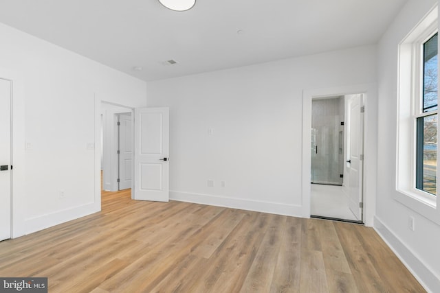 unfurnished bedroom with light wood finished floors, multiple windows, ensuite bath, and baseboards