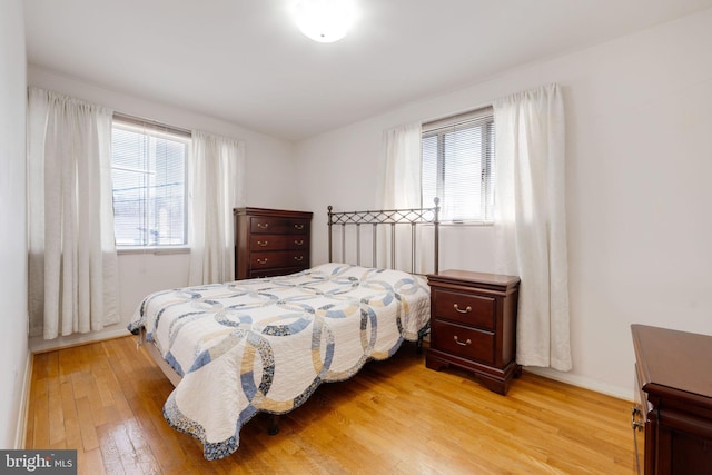 bedroom with multiple windows, light wood-style floors, and baseboards