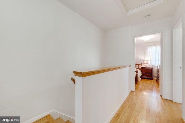 hallway featuring an upstairs landing, light wood-type flooring, and baseboards