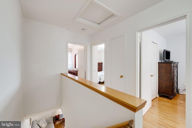 hallway featuring light wood-type flooring, an upstairs landing, and attic access