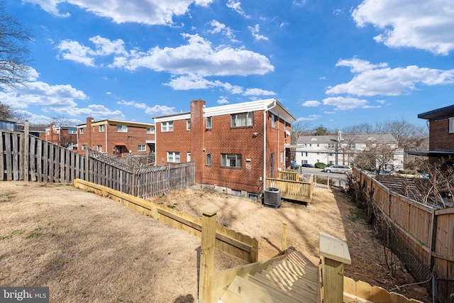 rear view of house with central AC unit, a fenced backyard, brick siding, and a residential view