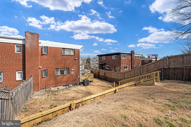 back of property with brick siding, central AC unit, a lawn, and a fenced backyard