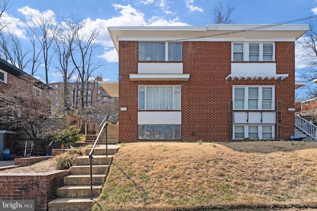 view of front of house with a front lawn, brick siding, and stairs