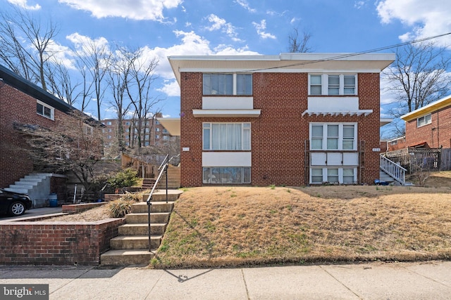 view of front of house with a front yard, stairway, and brick siding