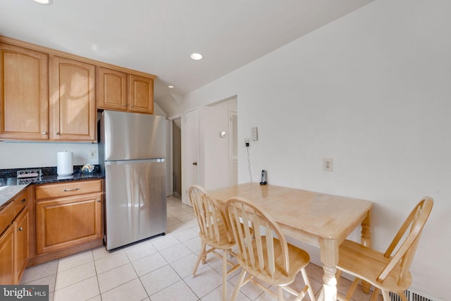 kitchen featuring dark stone countertops, freestanding refrigerator, recessed lighting, brown cabinetry, and light tile patterned floors