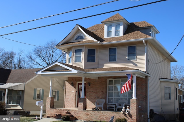 traditional style home with brick siding, covered porch, and a shingled roof