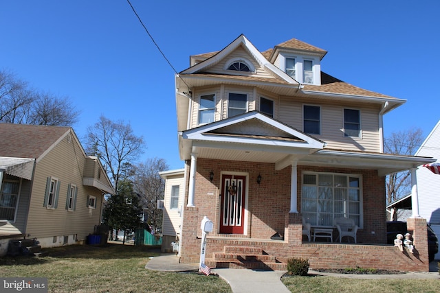 view of front facade featuring a front lawn, covered porch, brick siding, and a shingled roof