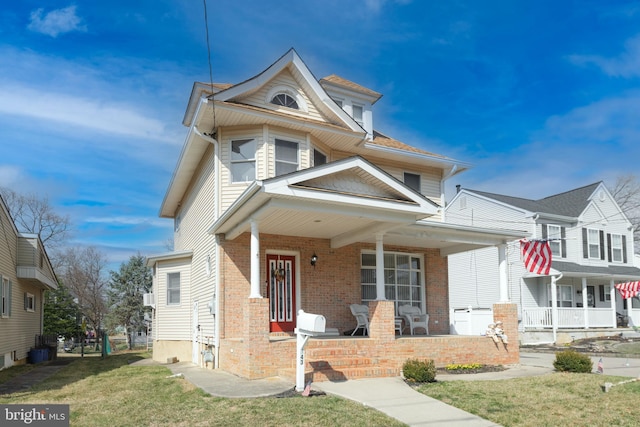 view of front of property with a front yard, brick siding, and covered porch