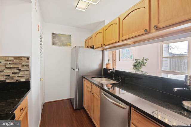 kitchen with dark wood finished floors, dark stone counters, a sink, decorative backsplash, and appliances with stainless steel finishes