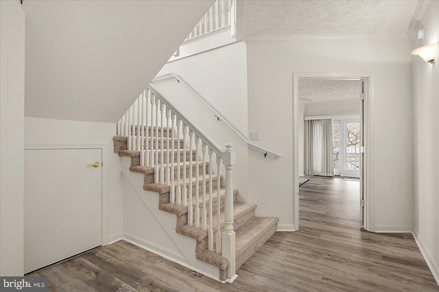 stairway featuring ornamental molding, a textured ceiling, baseboards, and wood finished floors