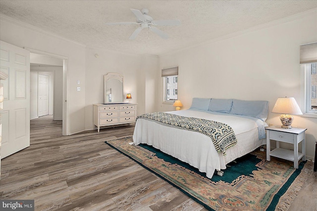 bedroom featuring wood finished floors, baseboards, ceiling fan, ornamental molding, and a textured ceiling