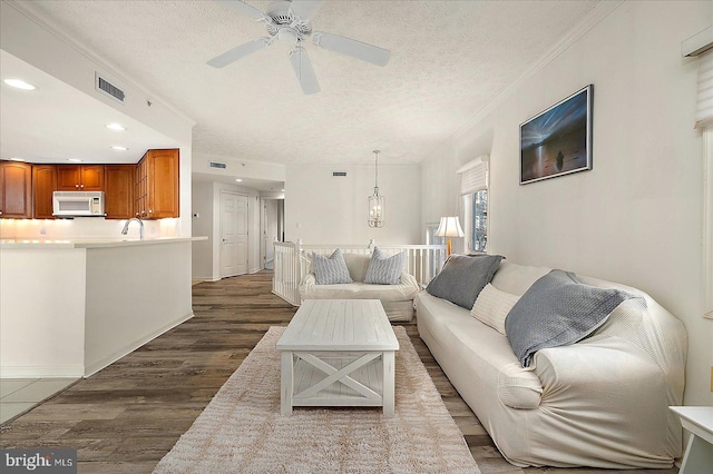 living area featuring visible vents, dark wood-type flooring, ornamental molding, recessed lighting, and a textured ceiling