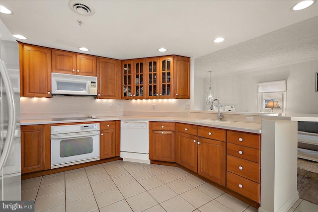 kitchen with brown cabinets, white appliances, a peninsula, and a sink