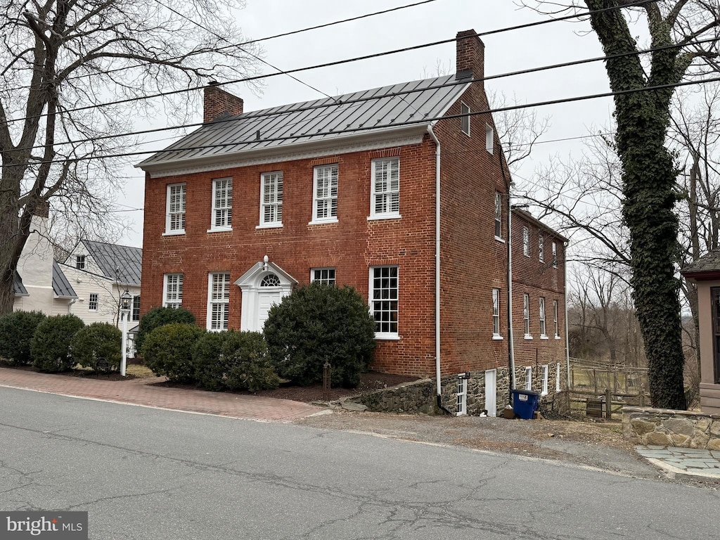 view of front of home with a standing seam roof, brick siding, and a chimney