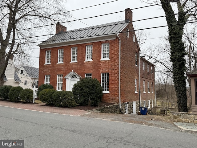 view of front of home with a standing seam roof, brick siding, and a chimney