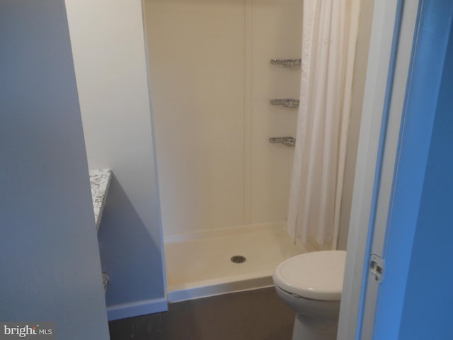 bathroom featuring toilet, baseboards, and a stall shower